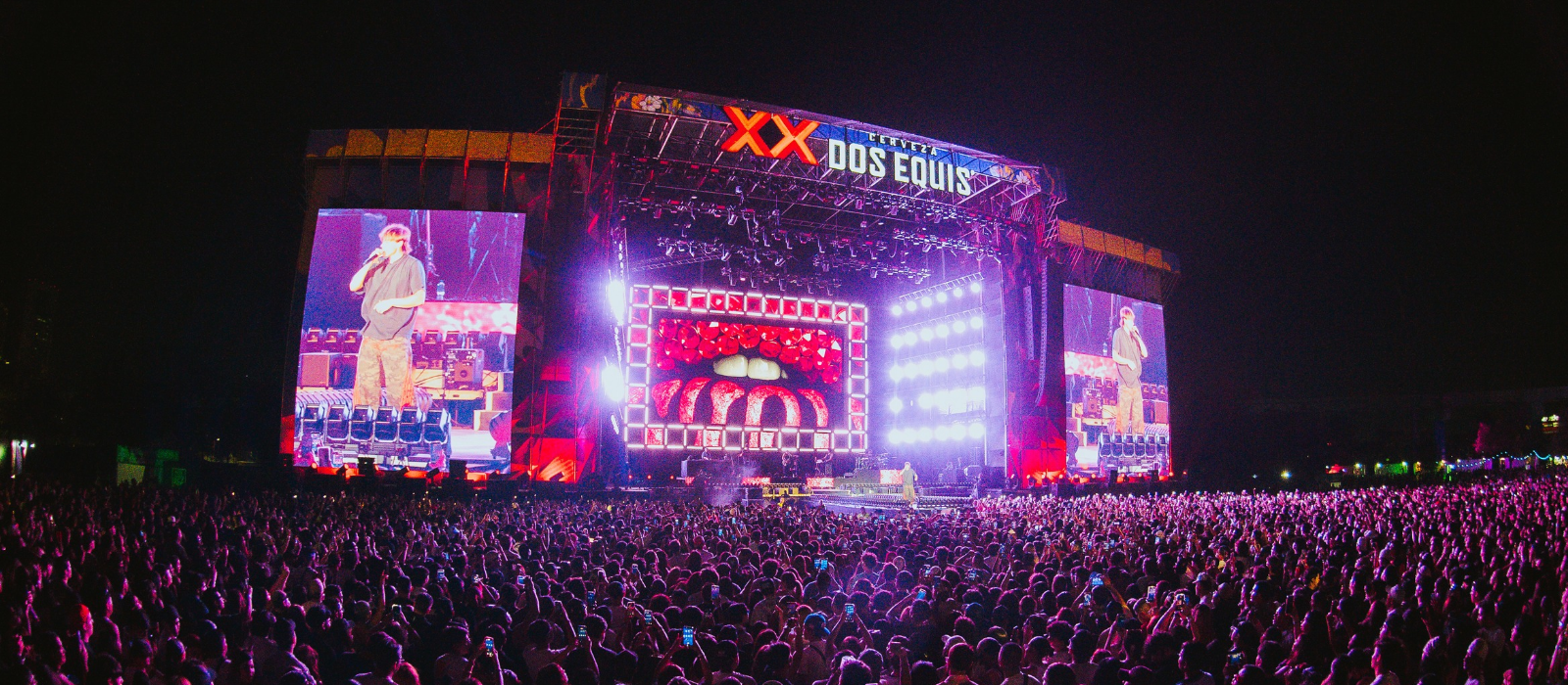Nighttime outdoor concert with a huge illuminated stage and a dense crowd watching a performance.